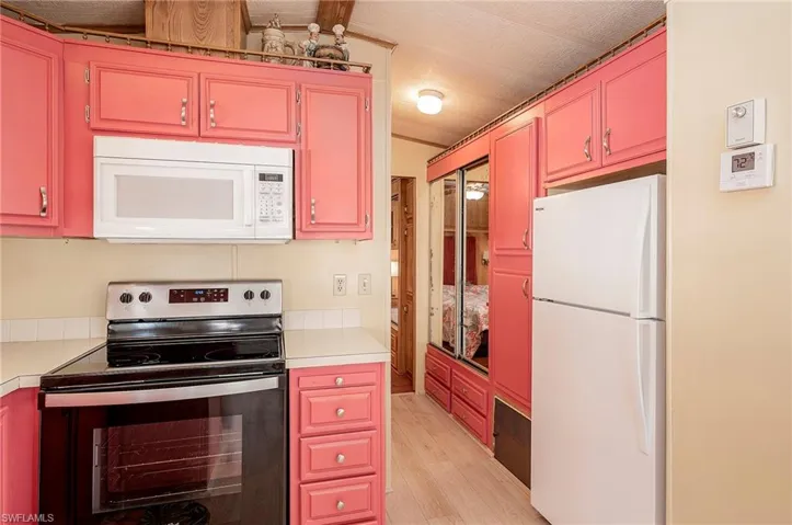 Kitchen with white appliances, light hardwood / wood-style flooring, and beamed ceiling