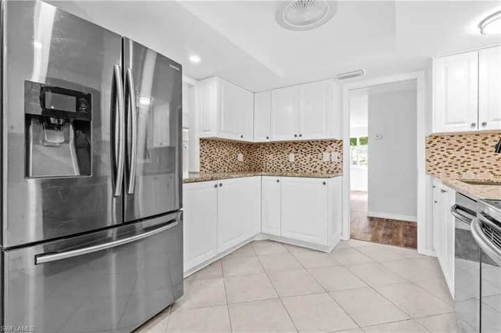 Kitchen featuring stainless steel appliances, white cabinetry, light stone countertops, light tile patterned floors, and a tray ceiling
