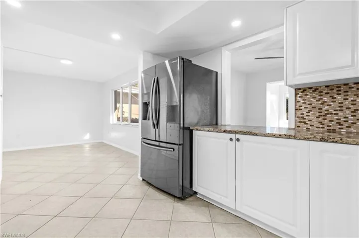Kitchen featuring stainless steel refrigerator with ice dispenser, dark stone countertops, white cabinets, tasteful backsplash, and light tile patterned flooring
