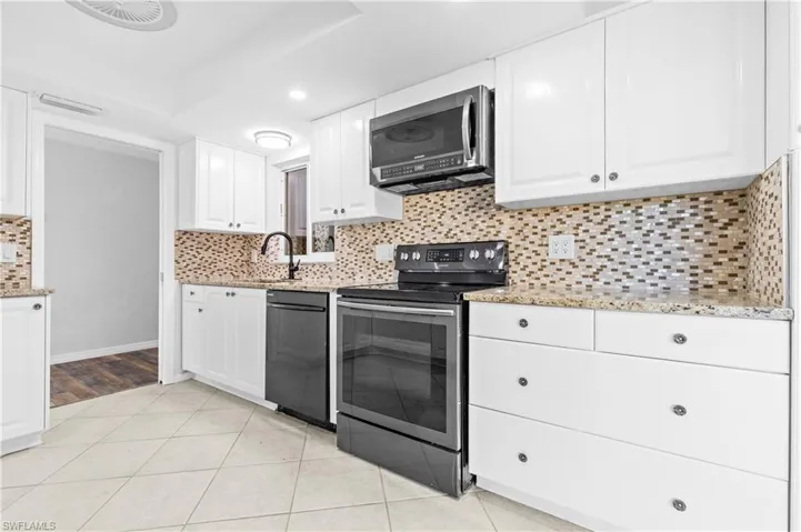 Kitchen with light stone countertops, stainless steel appliances, white cabinetry, light tile patterned floors, and backsplash