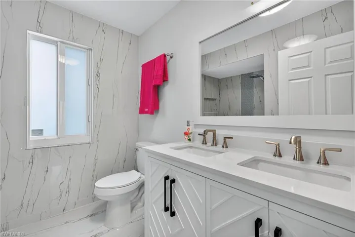 Full bath featuring marble finish floors, double vanity, and a marble finish shower