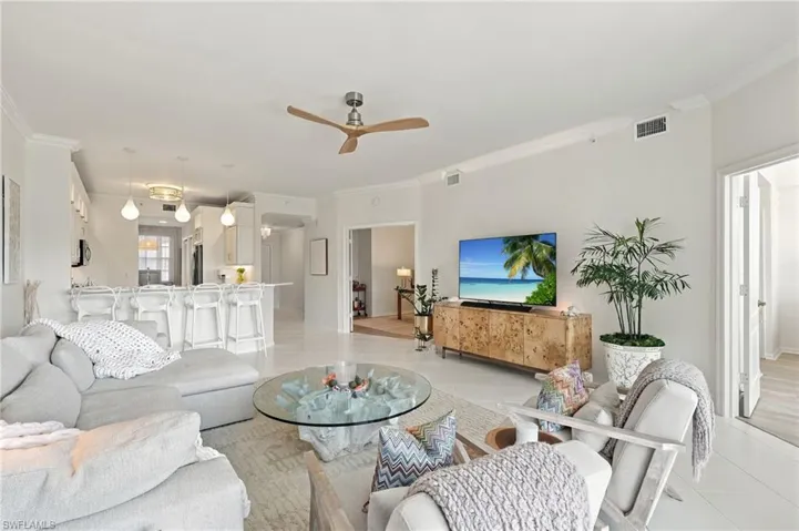 Open-concept living area featuring neutral wall color, crown molding, light-toned tile flooring, recessed ceiling lighting, and a three-blade ceiling fan