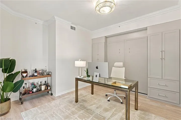 Custom built-in cabinetry featuring shaker-style doors, integrated crown molding, light-toned wood-finish flooring, and a decorative flush-mount ceiling fixture