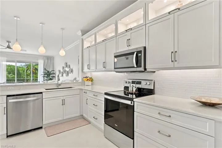 Kitchen featuring white shaker-style cabinetry with glass-front uppers, stone-finish countertops, stainless steel appliances, white subway tile backsplash, and three teardrop pendant lights