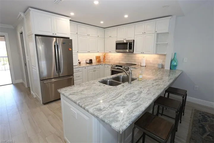 Kitchen with stainless steel appliances, a peninsula, white cabinets, backsplash, and recessed lighting