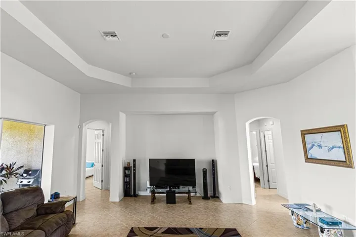 Living room with arched walkways, a tray ceiling, and light tile patterned floors