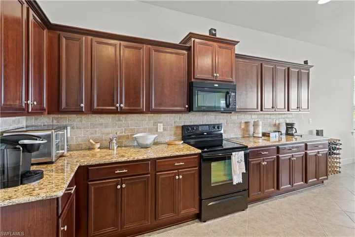 Kitchen featuring black appliances, light tile patterned floors, light stone counters, backsplash, and recessed lighting