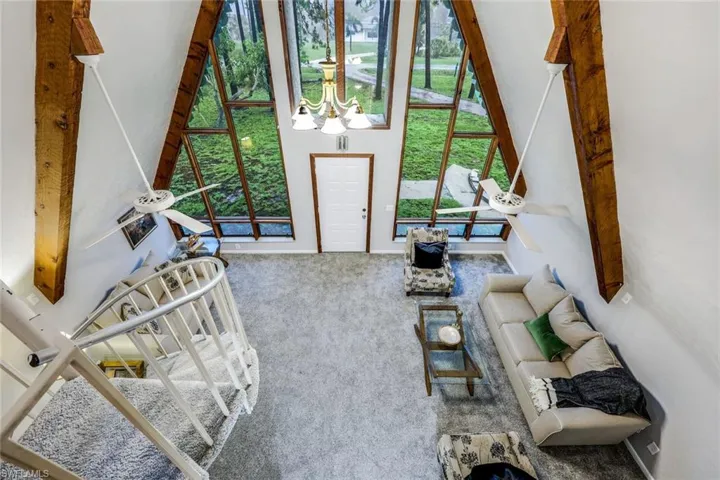 Carpeted living room with beamed ceiling, a notable chandelier, a wealth of natural light, and a high ceiling