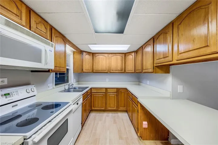 Kitchen featuring light hardwood / wood-style floors, sink, white appliances, and a drop ceiling