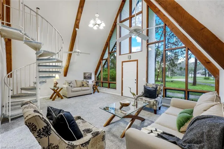 Carpeted living room featuring a wealth of natural light, beamed ceiling, a high ceiling, and ceiling fan with notable chandelier