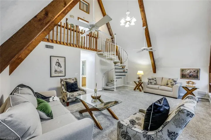 Living room with beam ceiling, a high ceiling, carpet flooring, and ceiling fan with notable chandelier