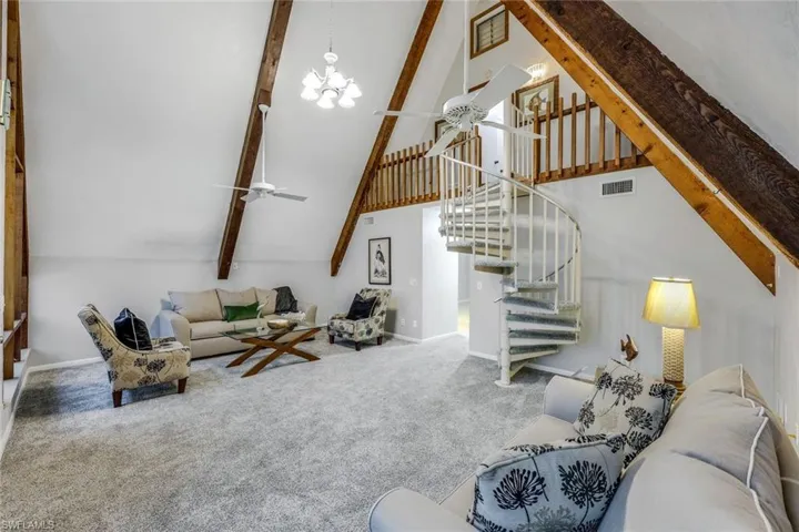 Carpeted living room with beam ceiling, high vaulted ceiling, and ceiling fan with notable chandelier