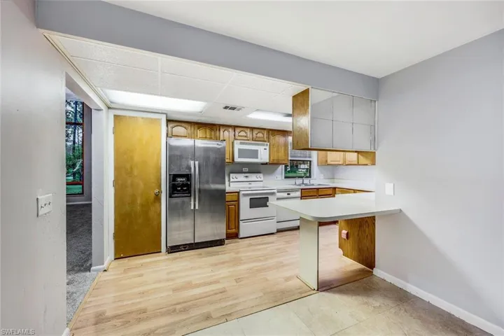 Kitchen featuring white appliances, kitchen peninsula, a drop ceiling, a breakfast bar, and sink
