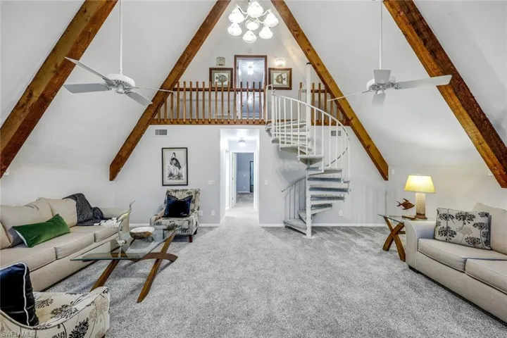 Carpeted living room with beamed ceiling, ceiling fan with notable chandelier, and high vaulted ceiling