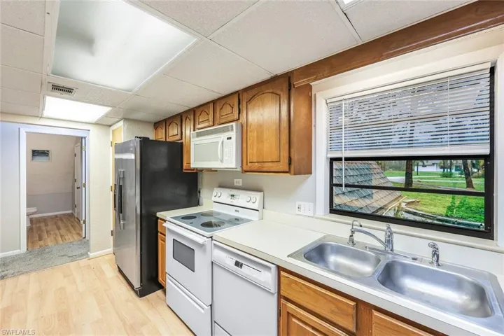 Kitchen with sink, a drop ceiling, white appliances, and light hardwood / wood-style flooring