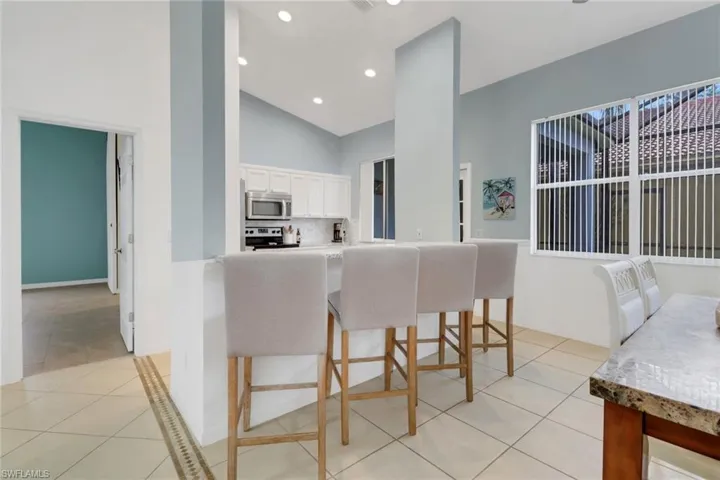 Kitchen featuring stainless steel microwave, light tile patterned floors, range with electric cooktop, white cabinetry, and high vaulted ceiling