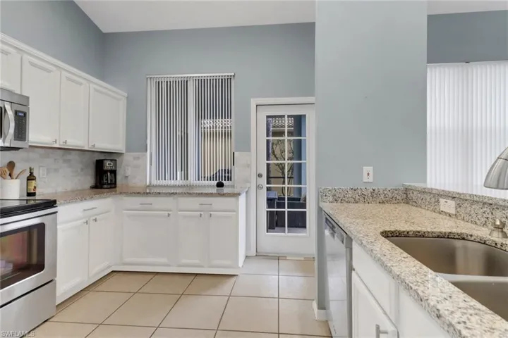 Kitchen with appliances with stainless steel finishes, light tile patterned floors, decorative backsplash, white cabinetry, and light stone counters