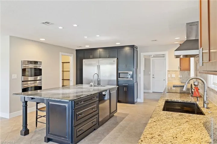 Kitchen featuring light stone counters, built in appliances, a breakfast bar area, island exhaust hood, and recessed lighting