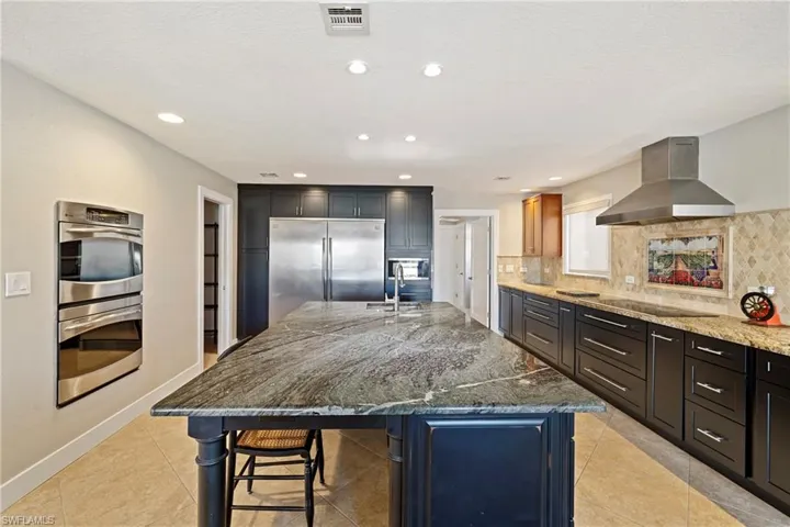Kitchen with dark stone counters, extractor fan, a kitchen island with sink, stainless steel appliances, and recessed lighting