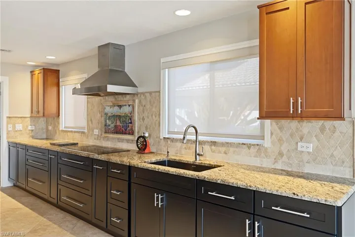 Kitchen with range hood, light stone counters, decorative backsplash, recessed lighting, and black electric stovetop