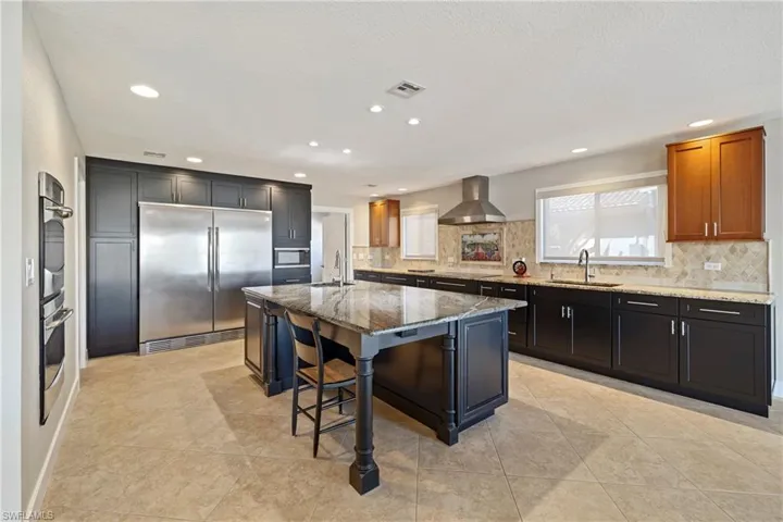 Kitchen with dark stone countertops, stainless steel appliances, a breakfast bar area, an island with sink, and backsplash