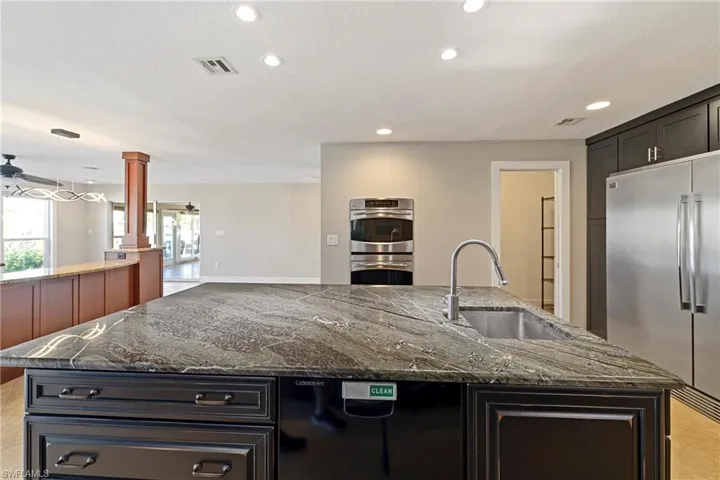 Kitchen with a kitchen island with sink, dark stone counters, dark cabinetry, stainless steel appliances, and recessed lighting