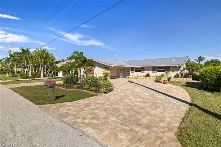Ranch-style home featuring a front lawn, decorative driveway, a garage, a metal roof, and stucco siding