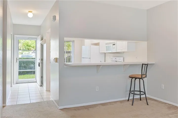 Kitchen with light tile patterned floors, light carpet, white appliances, a kitchen breakfast bar, and light countertops