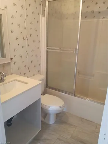 Full bathroom with wallpapered walls, vanity, and bath / shower combo with glass door