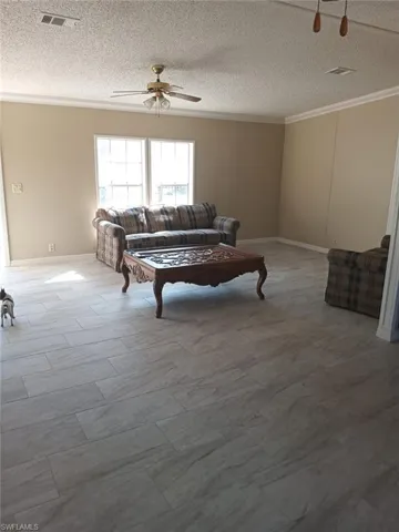 Living room featuring crown molding, ceiling fan, and a textured ceiling