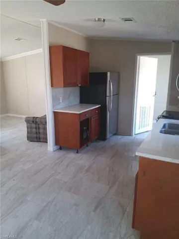 Kitchen featuring freestanding refrigerator, a textured ceiling, light countertops, crown molding, and brown cabinets