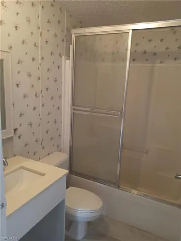 Full bathroom with wallpapered walls, vanity, enclosed tub / shower combo, and a textured ceiling
