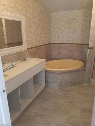 Full bathroom featuring wallpapered walls, tile walls, vanity, wainscoting, and a bath
