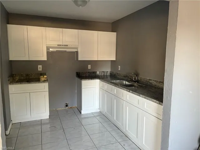 Kitchen featuring white cabinetry, dark stone countertops, under cabinet range hood, and light tile patterned flooring