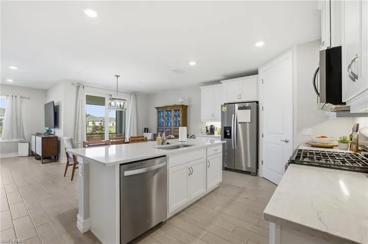 Kitchen with wood finish floors, stainless steel appliances, white cabinets, light stone counters, and hanging light fixtures