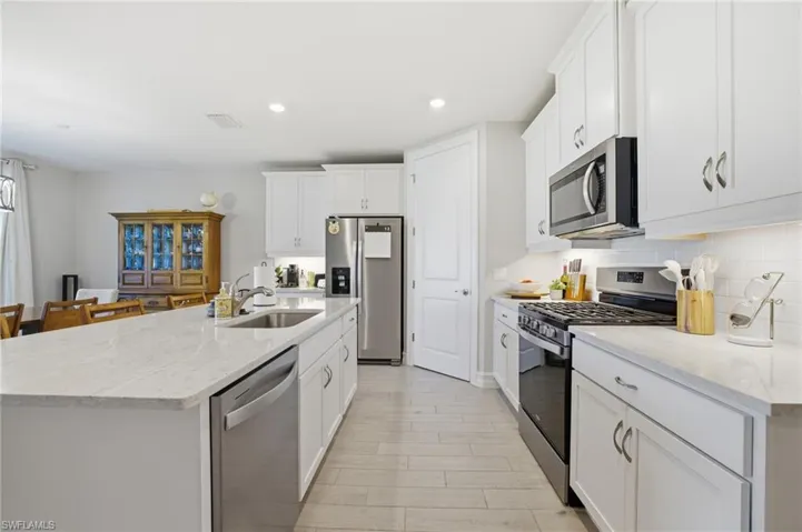 Kitchen with stainless steel appliances, light stone counters, white cabinetry, and recessed lighting