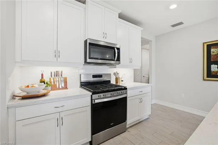 Kitchen with appliances with stainless steel finishes, white cabinets, decorative backsplash, light wood-style floors, and light stone countertops