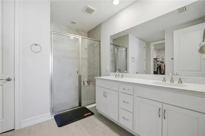 Bathroom with a walk in closet, double vanity, a shower stall, and wood tiled floors