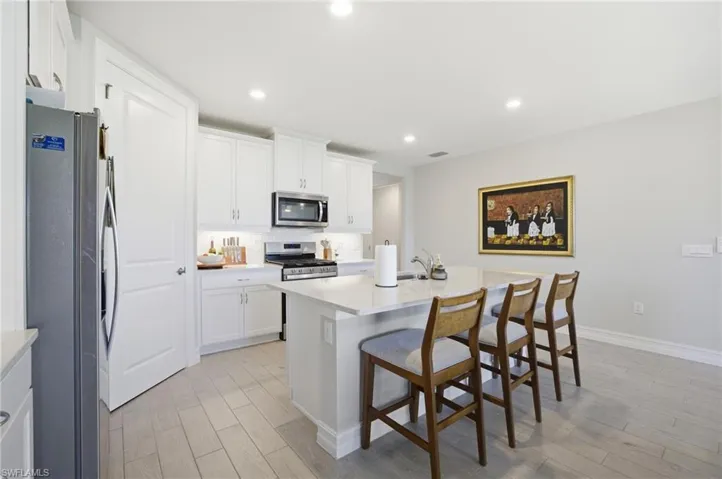 Kitchen featuring a breakfast bar area, stainless steel appliances, a center island with sink, white cabinetry, and recessed lighting