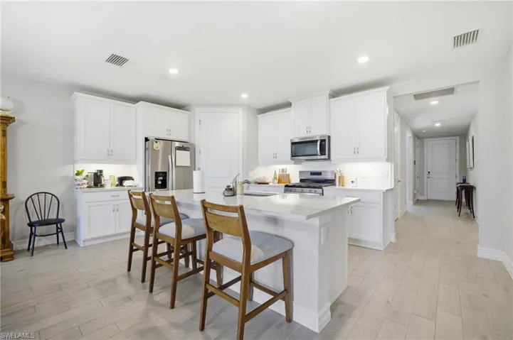 Kitchen featuring a breakfast bar area, white cabinetry, stainless steel appliances, an island with sink, and light wood finished floors