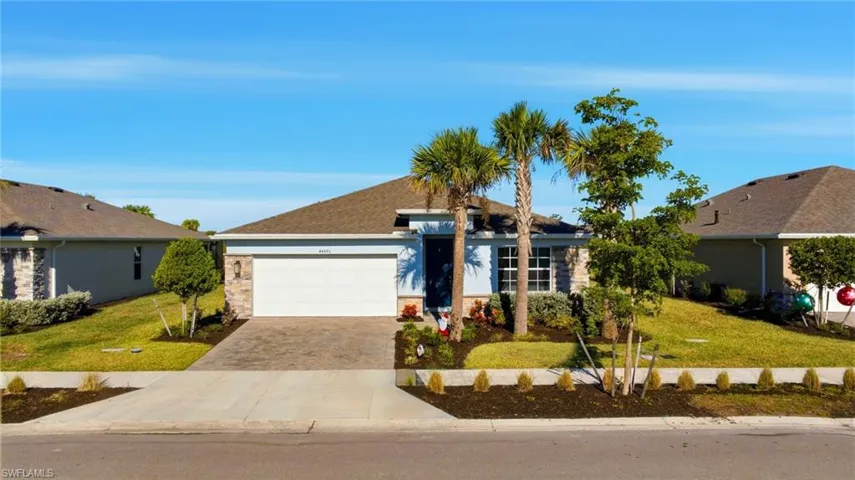 Single story home featuring a front lawn, driveway, stone siding, and an attached garage