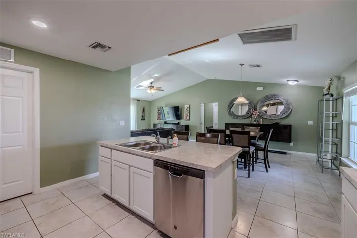 Kitchen featuring dishwasher, a sink, pendant lighting, vaulted ceiling, and white cabinets