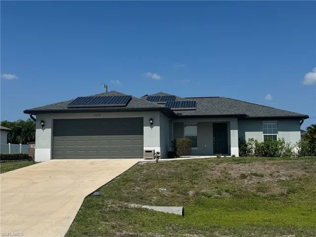 View of front of home with a garage, stucco siding, solar panels, concrete driveway, and a front lawn