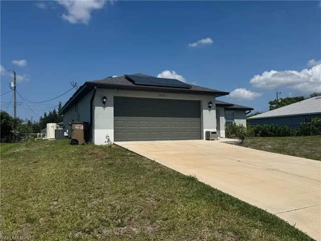View of front facade with roof mounted solar panels, concrete driveway, an attached garage, a front yard, and stucco siding