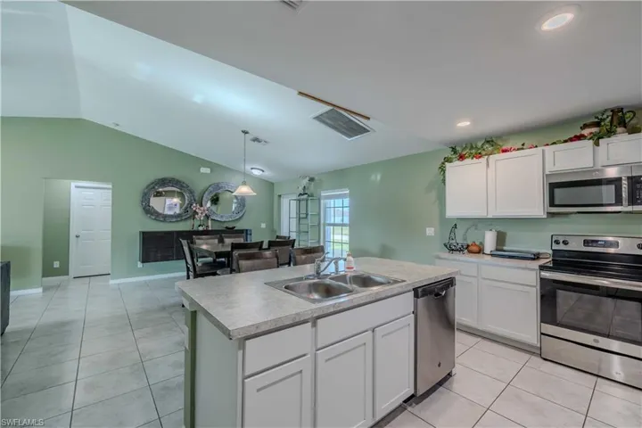 Kitchen with stainless steel appliances, a sink, vaulted ceiling, light tile patterned floors, and white cabinetry