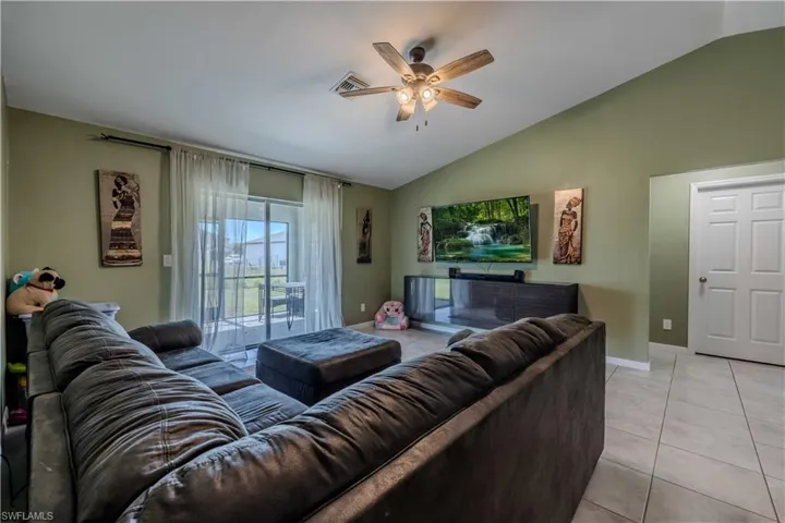 Living room featuring vaulted ceiling, a ceiling fan, baseboards, and light tile patterned floors