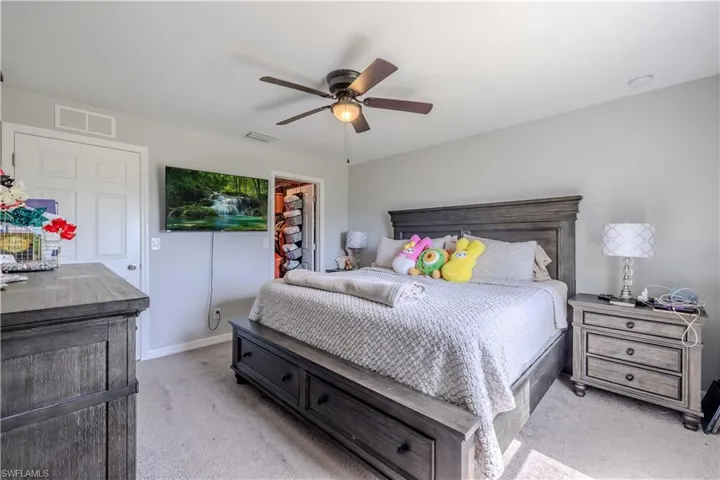 Bedroom featuring light colored carpet, a walk in closet, ceiling fan, a closet, and baseboards