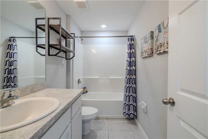 Bathroom with vanity, shower / tub combo, toilet, tile patterned floors, and baseboards