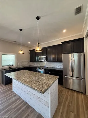 Kitchen with fridge, a center island, dark stone counters, dark wood-style flooring, and black range