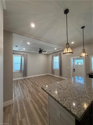 Kitchen featuring a center island, light stone countertops, dark wood-style flooring, a ceiling fan, and pendant lighting